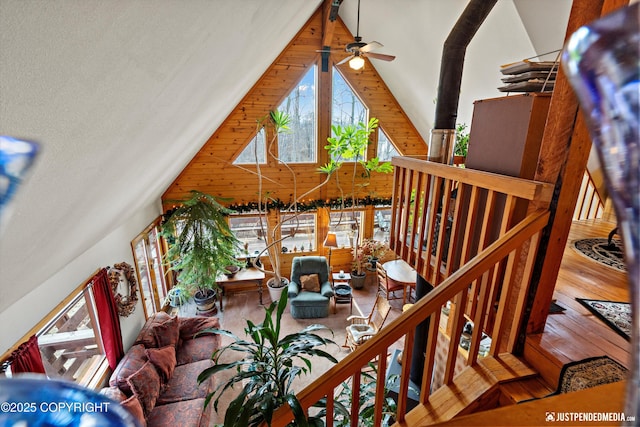 living room featuring ceiling fan, high vaulted ceiling, wood finished floors, and wooden walls