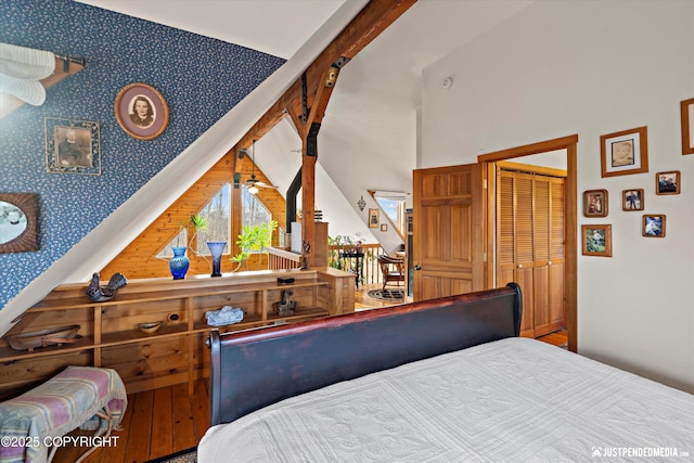 bedroom with an accent wall, high vaulted ceiling, and wallpapered walls