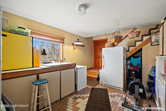 kitchen featuring fridge, freestanding refrigerator, white cabinets, and decorative light fixtures