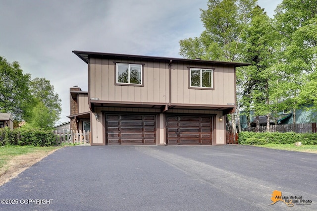 view of front facade with driveway, a chimney, an attached garage, and fence