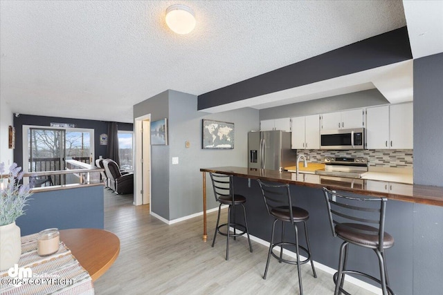 kitchen with appliances with stainless steel finishes, tasteful backsplash, a breakfast bar area, light hardwood / wood-style floors, and white cabinetry