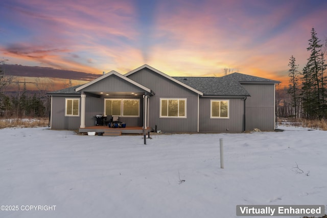 snow covered rear of property featuring a deck and a shingled roof