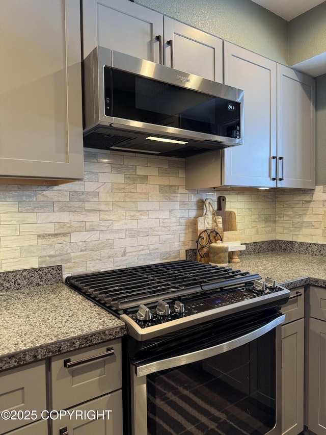 kitchen featuring gray cabinetry, appliances with stainless steel finishes, light stone counters, and decorative backsplash