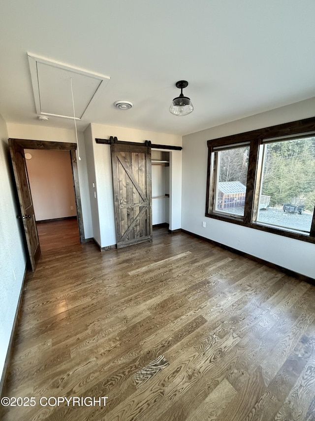 unfurnished bedroom with a barn door and dark hardwood / wood-style flooring