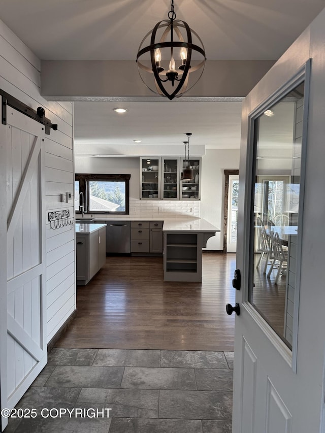 kitchen with stainless steel dishwasher, a barn door, hanging light fixtures, and gray cabinetry