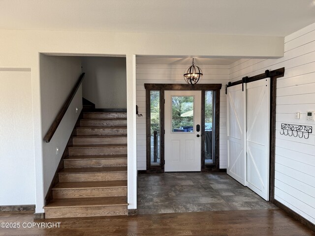 foyer featuring a barn door, dark hardwood / wood-style floors, a notable chandelier, and wood walls