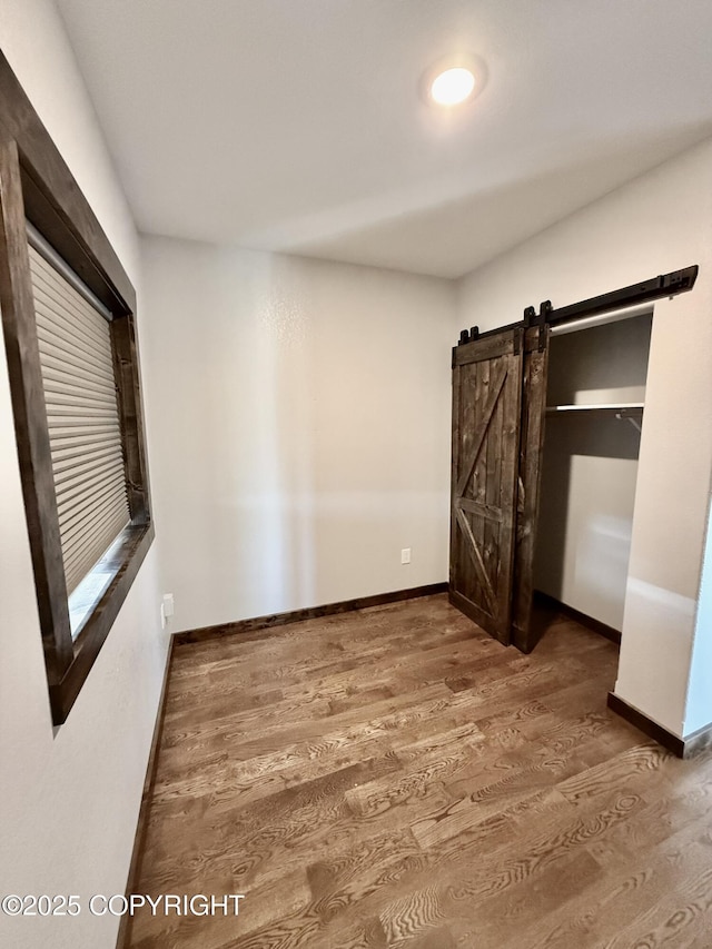 unfurnished bedroom with a barn door and dark hardwood / wood-style floors