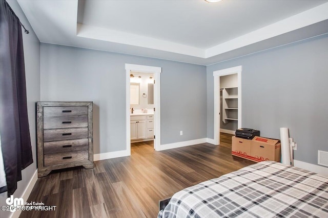 bedroom with a raised ceiling, a walk in closet, dark hardwood / wood-style floors, and ensuite bath