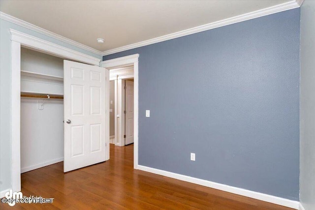 unfurnished bedroom with a closet, dark hardwood / wood-style flooring, and ornamental molding