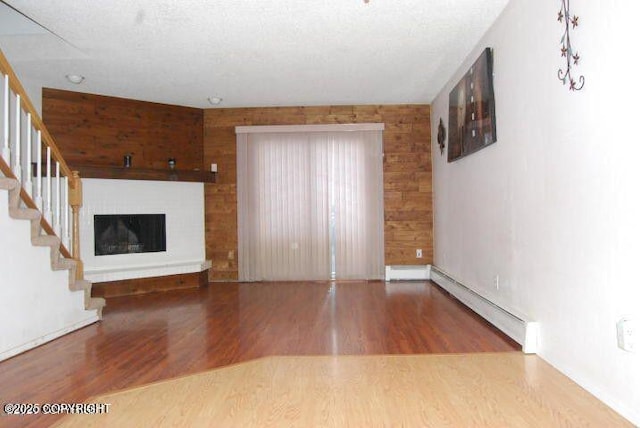 unfurnished living room featuring wood-type flooring, a brick fireplace, a baseboard heating unit, and a textured ceiling