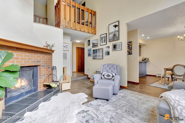 living area featuring wood finished floors, baseboards, a tile fireplace, a towering ceiling, and a notable chandelier