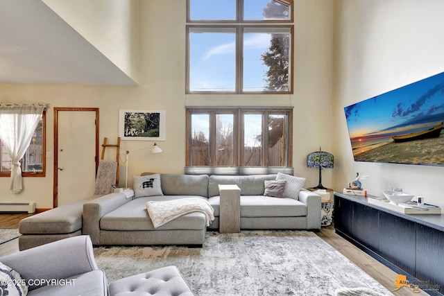 living room with a baseboard heating unit, wood finished floors, and a towering ceiling