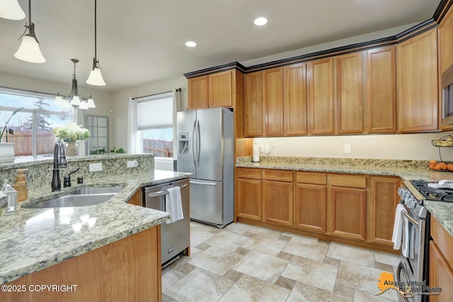 kitchen featuring brown cabinetry, stainless steel appliances, a sink, and decorative light fixtures