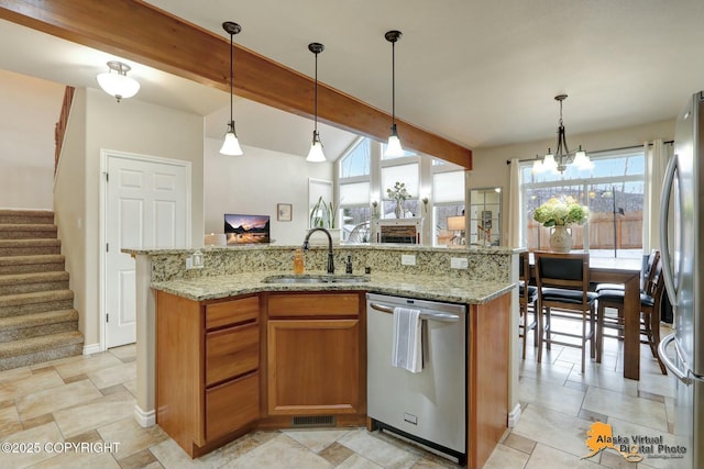 kitchen featuring brown cabinets, beamed ceiling, a kitchen island with sink, stainless steel appliances, and a sink