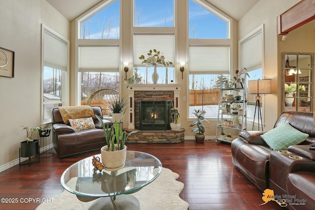 living room featuring dark wood-style floors, baseboards, high vaulted ceiling, and a stone fireplace