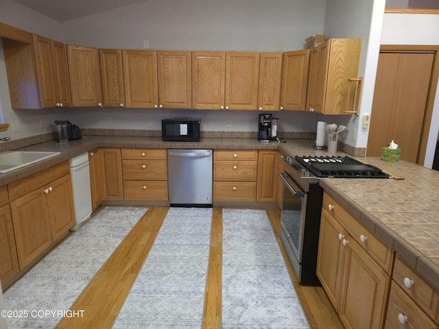 kitchen featuring light wood-type flooring, tile countertops, lofted ceiling, stainless steel appliances, and sink