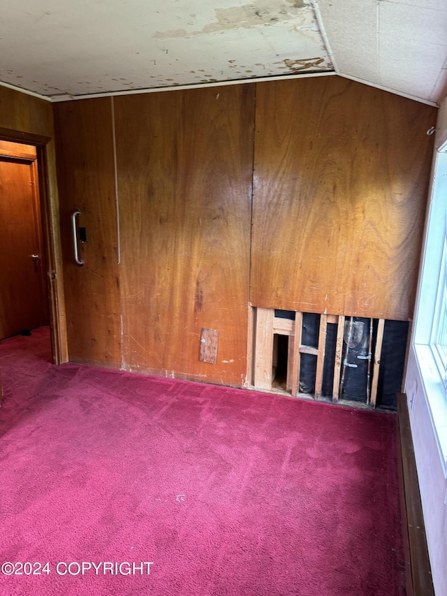 carpeted spare room featuring lofted ceiling and wooden walls