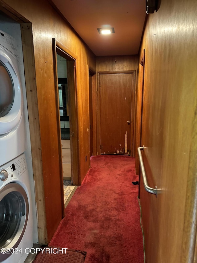 corridor with wood walls, carpet floors, and stacked washing maching and dryer