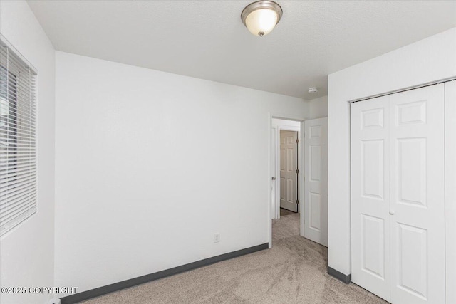 unfurnished bedroom featuring light carpet, a textured ceiling, baseboards, and a closet