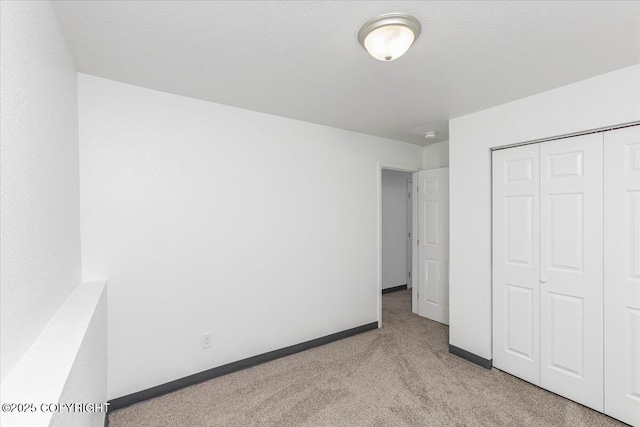 unfurnished bedroom with light carpet, a textured ceiling, baseboards, and a closet