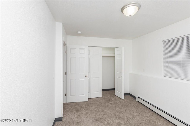 unfurnished bedroom featuring a baseboard heating unit, a closet, light carpet, and baseboards