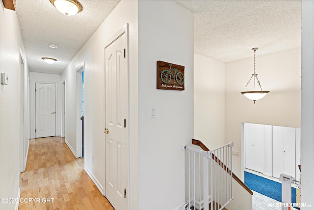 hallway with baseboards, light wood finished floors, an upstairs landing, and a textured ceiling