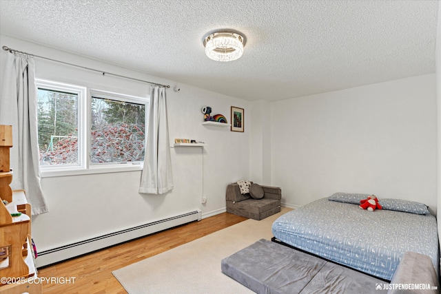 bedroom with a textured ceiling, baseboard heating, wood finished floors, and baseboards