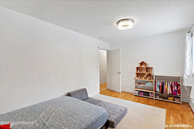 bedroom featuring a textured ceiling, baseboards, baseboard heating, and wood finished floors