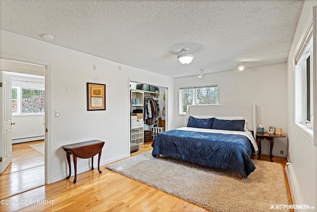 bedroom with a textured ceiling, a closet, a baseboard heating unit, and wood finished floors