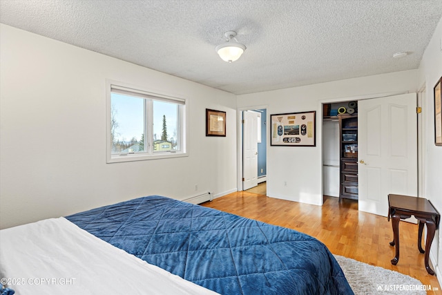 bedroom featuring a textured ceiling, a baseboard heating unit, and wood finished floors