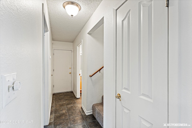 corridor with a textured ceiling, a textured wall, stairs, and baseboards