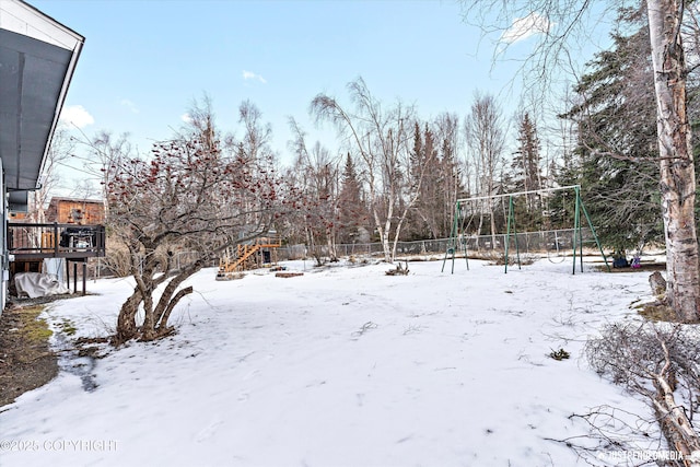 snowy yard with playground community, fence, and a deck