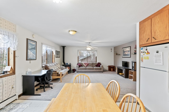 dining space featuring a wood stove, a healthy amount of sunlight, baseboard heating, and light colored carpet