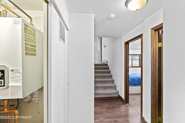 hall with water heater, stairway, a textured ceiling, and dark wood finished floors