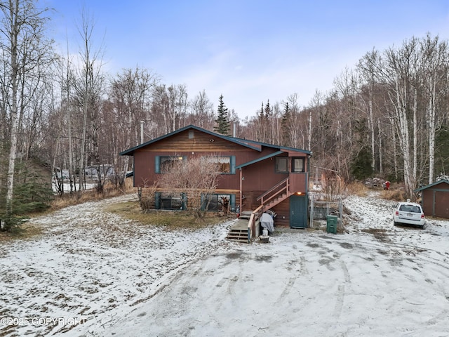 snow covered back of property with a garage and stairway