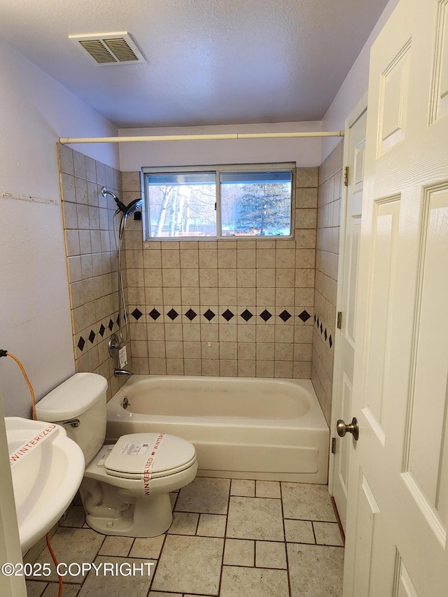 full bathroom with sink, tiled shower / bath, toilet, and a textured ceiling