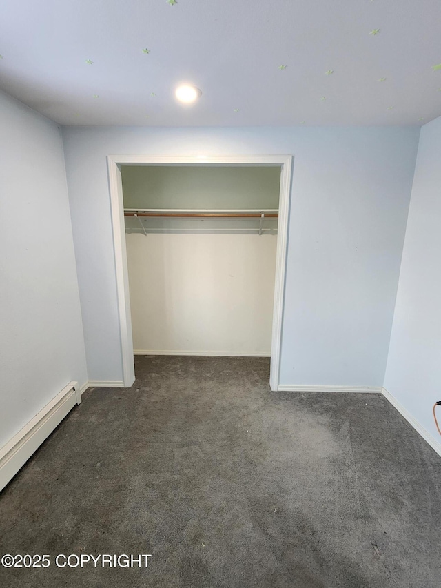 unfurnished bedroom with baseboard heating, dark colored carpet, and a closet