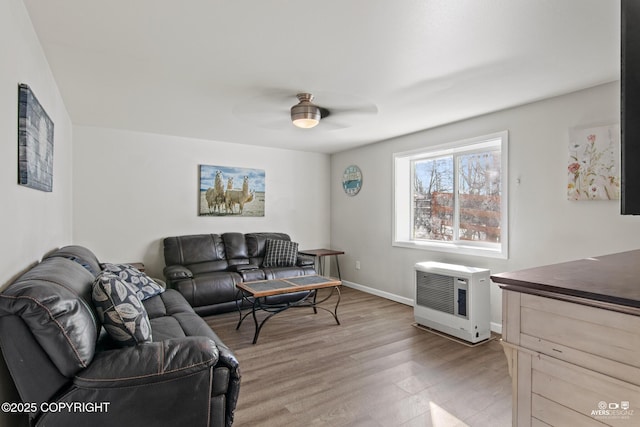 living area with baseboards, light wood finished floors, a ceiling fan, and heating unit