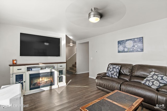 living area with a glass covered fireplace, stairway, wood finished floors, and baseboards