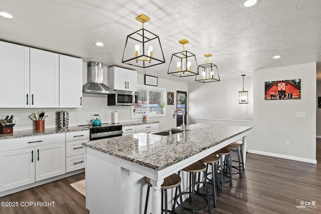 kitchen with stainless steel microwave, a sink, wall chimney range hood, and a textured ceiling