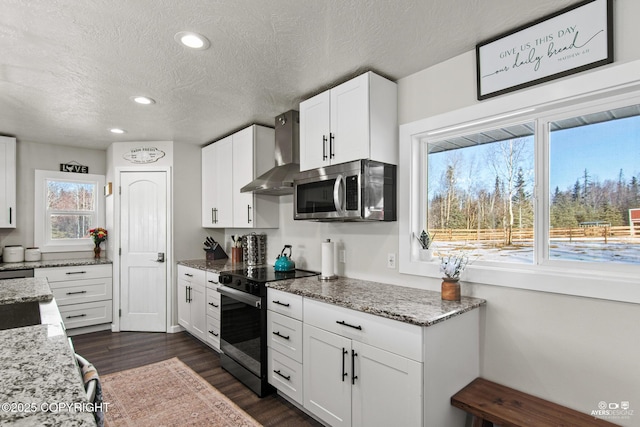 kitchen with dark wood-style floors, wall chimney exhaust hood, stainless steel microwave, white cabinetry, and range with electric stovetop