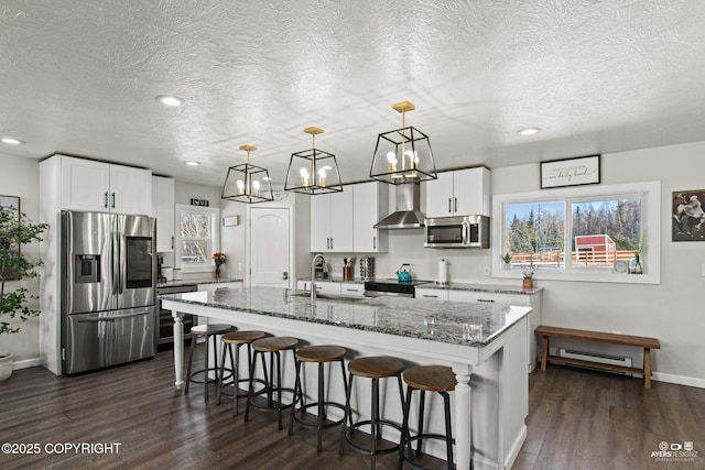 kitchen with stainless steel appliances, wall chimney range hood, stone counters, and dark wood-type flooring