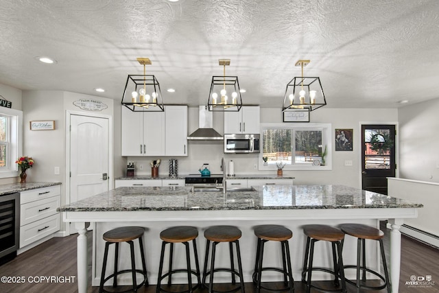 kitchen featuring a breakfast bar area, a sink, wall chimney range hood, stainless steel microwave, and dark wood finished floors