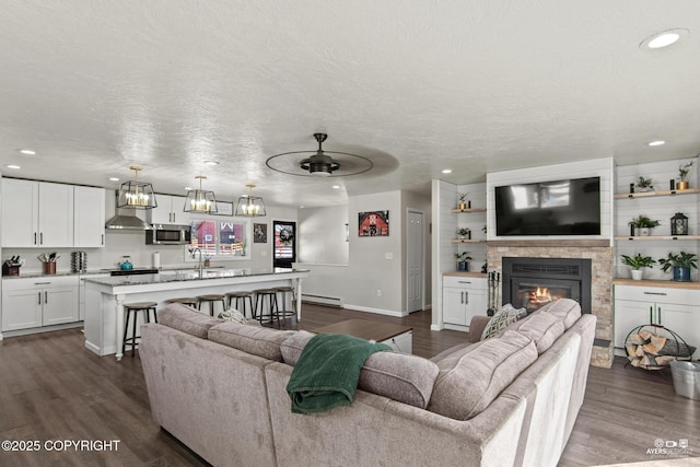 living area with a glass covered fireplace, a baseboard radiator, dark wood-style flooring, a textured ceiling, and recessed lighting