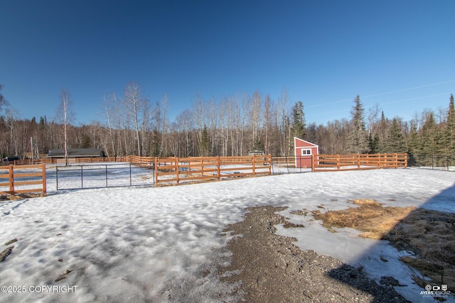 yard covered in snow with an outdoor structure, an enclosed area, a wooded view, and fence