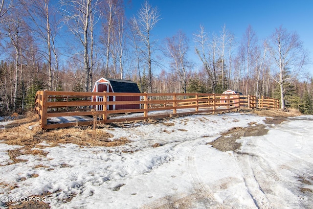 yard covered in snow with an outbuilding, a forest view, a barn, and fence