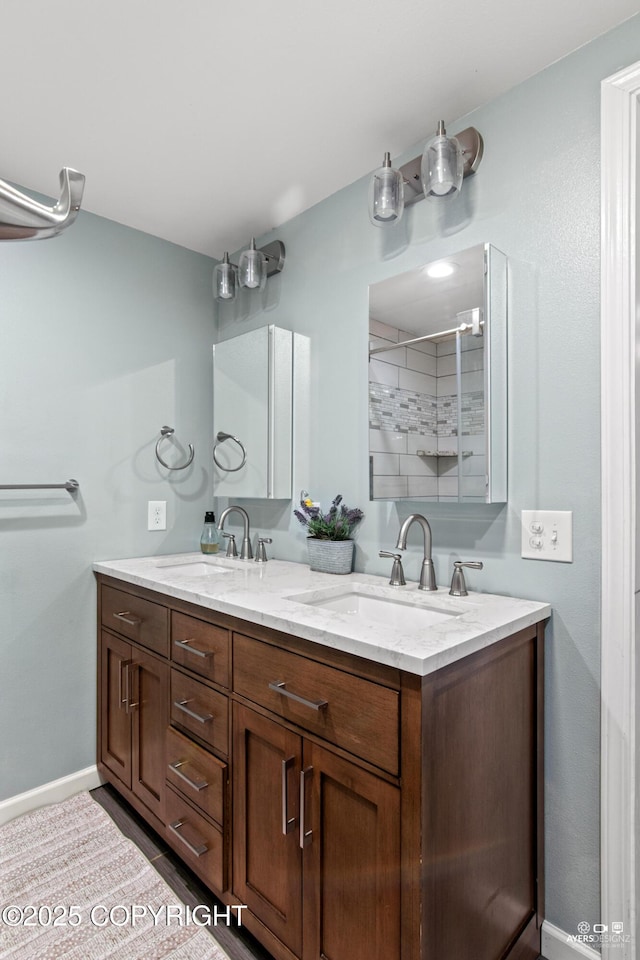 full bath with double vanity, a shower, a sink, and baseboards