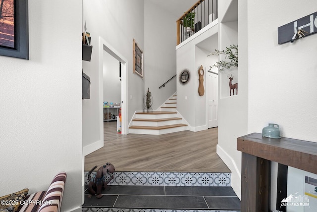 foyer entrance with stairs, wood finished floors, baseboards, and a towering ceiling