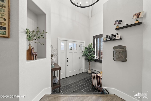 entrance foyer featuring baseboards, wood tiled floor, a chandelier, baseboard heating, and a high ceiling