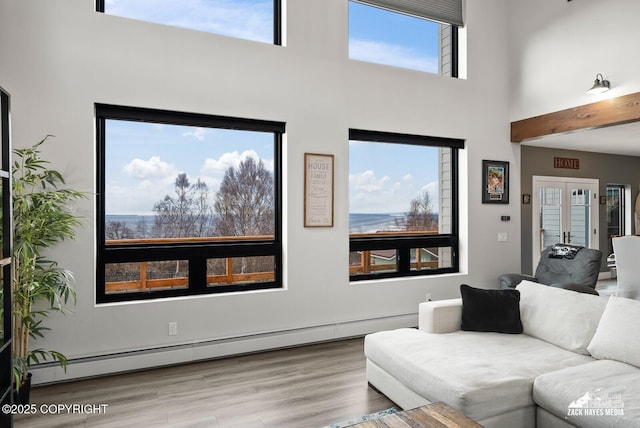 living room featuring a baseboard heating unit, a high ceiling, wood finished floors, and french doors